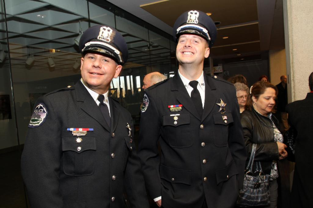 Zwei grinsende Beamte vorne, Menschen in der Mitte, Glasfenster links, Lampen und Decke oben und Säulen und Menschen rechts.