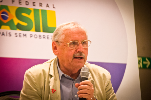 Eine Person, die in ein Mikrofon spricht und im Hintergrund ein Banner mit der Aufschrift 'Bundes' hält.