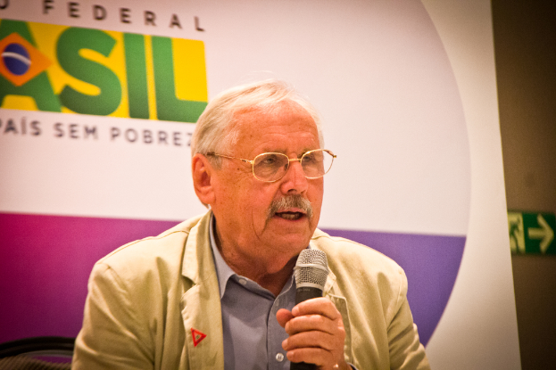 Eine Person, die in ein Mikrofon spricht und im Hintergrund ein Banner mit der Aufschrift 'Bundes' hält.