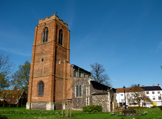 Eine grasbewachsene Fläche mit einem Pfahl, Gebäuden und Bäumen im Hintergrund.