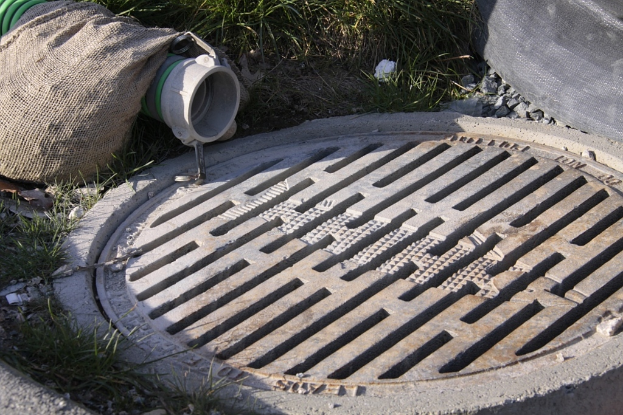 Ein Schlagloch mit Gras, Steinen, einer Tasche und einem Rohr auf der linken Seite und Gras, Steinen und einem Objekt oben.