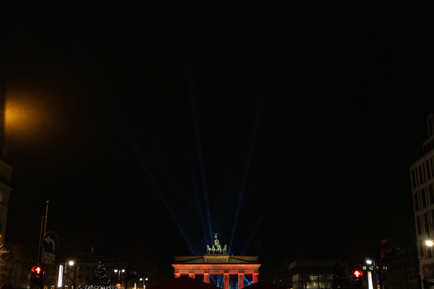 Brandenburger Tor bei Nacht, beleuchtet von Straßenlaternen, mit umliegenden Gebäuden, Bäumen, Pfählen, Verkehrszeichen, Schildern und Zelten unter einem dunklen Himmel.