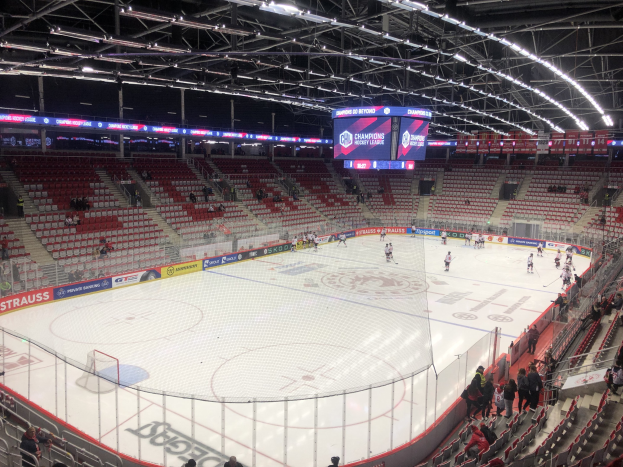 Eishockeyspiel in einer großen Arena zwischen den St. Louis Blues und Detroit Red Wings, mit Zuschauern auf den Sitzplätzen und in der Nähe des Spielfelds, umgeben von einem Zaun und einem Bildschirm.