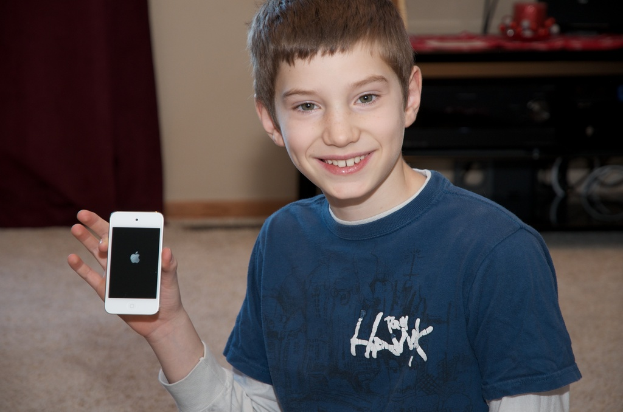 Ein Junge h√∂lt ein Mobiltelefon vor einer Wand.