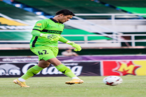 Ein Torwart in einem grünen Trikot schießt einen Fußball auf einem Rasenfeld in einem Stadion, mit Bannern im Hintergrund, die 'Chivas USA gegen Mexico City, 3-1, Copa Libertadores' lesen.