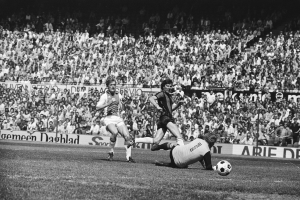 Schwarzes Foto von Fußballspielern im Einsatz auf einem Feld mit Zuschauern im Hintergrund und einem Bundesliga 1978-79 Ajax vs. Hannover 96-Banner.