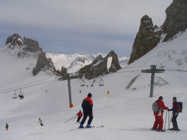Menschen in Pullovern fahren mit einer Seilbahn auf Eis, Berge und einen bewölkten Himmel im Hintergrund.