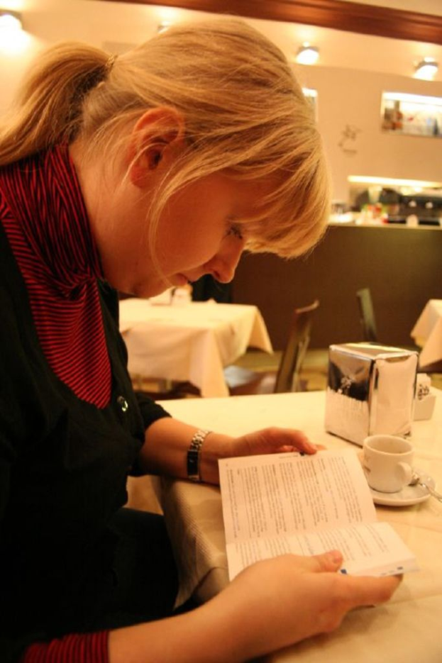 Eine Frau sitzt auf einem Stuhl und hält ein Buch auf einem Tisch, auf dem auch eine Tasse und ein Fußball sind.