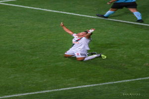 Ein Fußballspieler kniet auf dem Boden und streckt die Arme aus, um zu feiern, trägt eine Sportuniform und Schuhe.