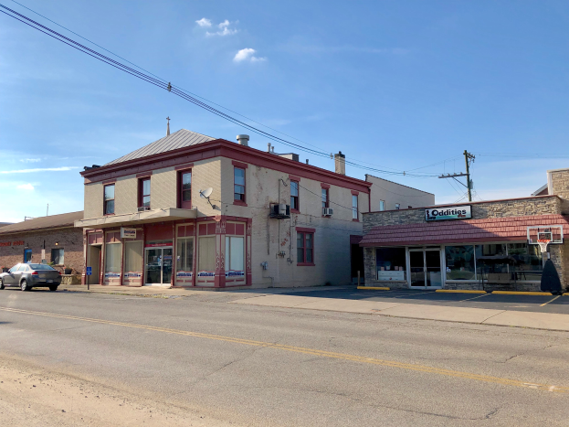 Ein Gewerbeobjekt zum Verkauf an 715 N Main Street, mit einem Gebäude mit Fenstern, Türen und Texttafeln, einem parkenden Auto an der Straßenseite und Strommasten mit Drähten im Hintergrund unter einem bewölkten Himmel.