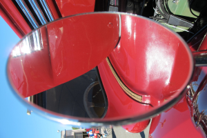 Ein Vergrößerungsglas zeigt das Lenkrad eines roten Autos, mit dem Auto und den umliegenden Gebäuden und Bäumen im Hintergrund.