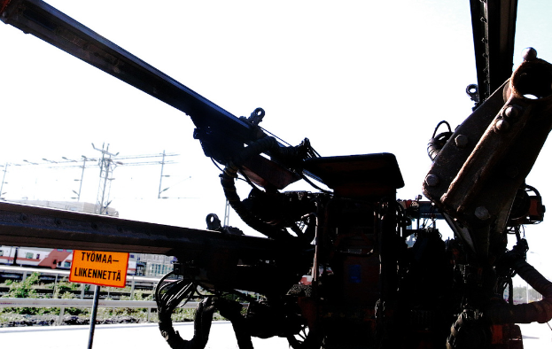 Eine Maschine ist im Vordergrund mit Strommasten, Kabeln, Barrieren, Pflanzen und Himmel im Hintergrund.