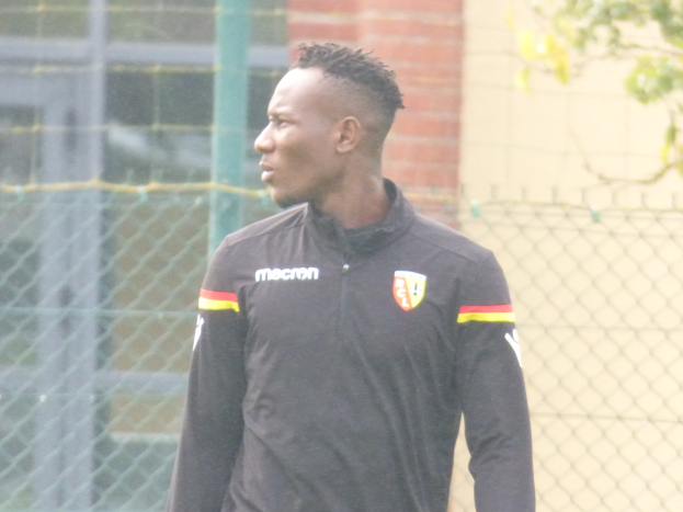 Ein Mann In Einer Schwarzen Jacke Steht Auf Einem Fussballfeld Umgeben Von Einem Zaun Und Einem Baum Und Sieht konzentriert Aus