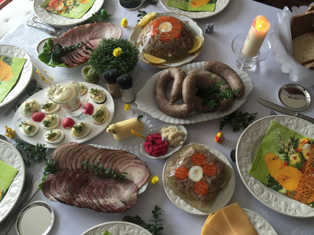 Ein lang gedeckter Tisch mit verschiedenen Gerichten, Besteck und Kerzen, umgeben von Stühlen, der auf ein traditionelles deutsches Osteressen hinweist.