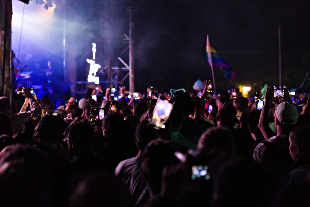 Menge bei einem Konzert mit hochgehaltenen Handys, beleuchtet von Lichtern, umgeben von Pfählen und einer Fahne.