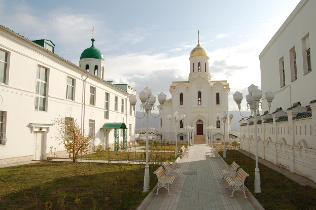 Eine Stadtansicht mit Gebäuden mit sichtbaren Fenstern, einer grünen Fläche mit einem Lichtmast, Blumenkasten und Bänken, einem Fußweg und einem bewölkten Himmel.