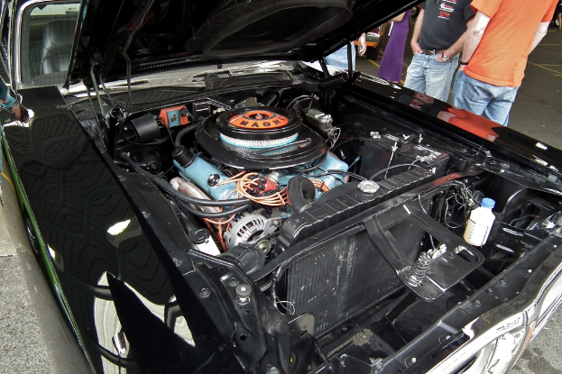 Nahaufnahme einer Autofront mit sichtbaren Teilen, mit unscharfen Menschen und einer Straße im Hintergrund.