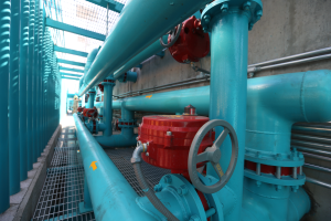 Eine große Gruppe von blauen Rohren und Ventilen in einem Gebäude, mit einem prominenten roten Ventil in der Mitte, Metallstangen links und einer Wand im Hintergrund, die wahrscheinlich den Bau einer Gasleitung darstellt.