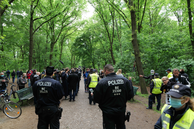Polizisten vor einer Menschenmenge bei einer Outdoor-Veranstaltung, mit Fahrrädern und einer Bank im Vordergrund.