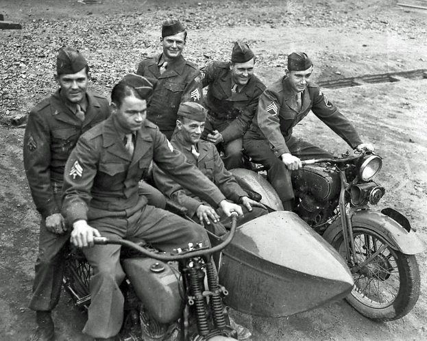 Eine Gruppe von Männern auf Fahrrädern sitzend, lachend, auf einer Straße, in einem Schwarz-Weiß-Foto.
