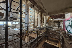 Verlassene Gebäudeinneres mit Graffiti-bedeckten Wänden, bröckelnden Strukturen, Geländern, Pfählen, Rohren und zerbrochenen Fenstern, mit einem Wasserzeichen unten.