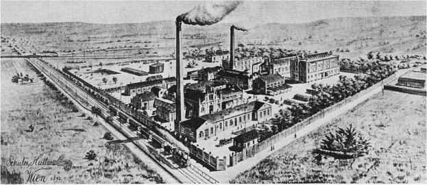 Ein altes Schwarz-Weiß-Luftbild der Wien, Illinois-Fabrik mit Rauch aus den Schornsteinen, umgeben von Gebäuden, Bäumen, Straßen, Fahrzeugen und Hügeln.