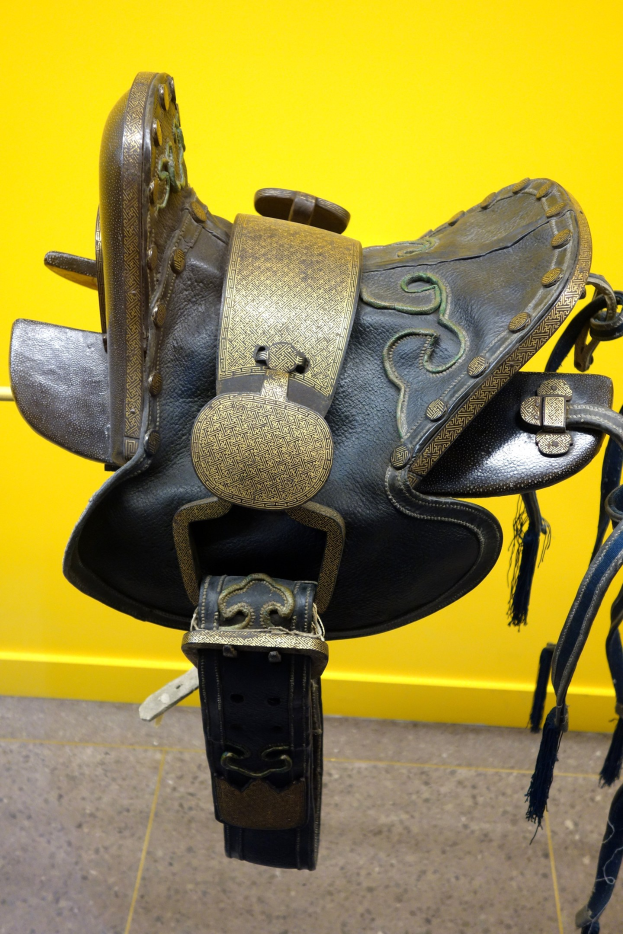 Nahaufnahme eines Pferdesattels, der auf einer gelben Wand mit dem Boden darunter zur Schau gestellt wird.