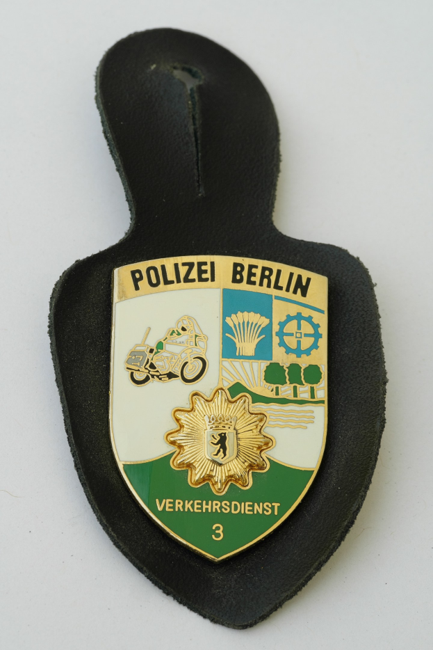 Ein schildförmiges Polizeibadge mit der Aufschrift "Polizei Berlin" auf einem blauen Hintergrund, einem weißen Rand, einem weißen Stern in der Mitte und schwarzer fetter Schrift auf einer Oberfläche.