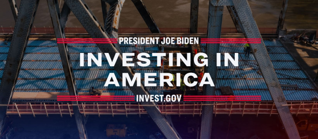 Präsident Joe Biden steht mit einer Brücke im Hintergrund, umgeben von verstreuten Gegenständen, mit dem prominenten Text "In Amerika investieren".