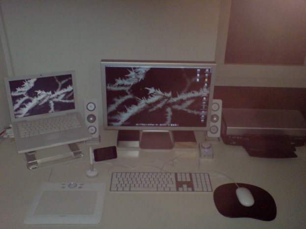 Ein Monitor, Laptop, Tastatur, Maus und andere elektronische Geräte sind auf einem Schreibtisch angeordnet.