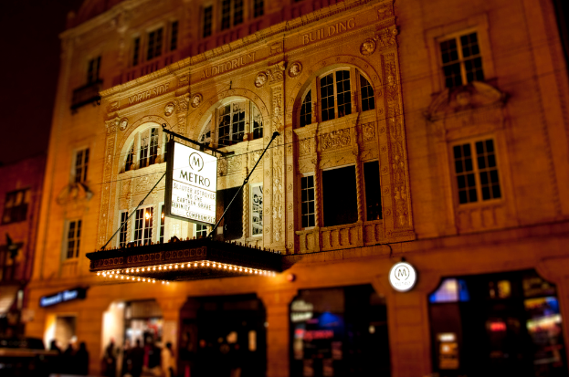 Ein gelbes Gebäude mit Geschäften im Erdgeschoss, eines davon hat ein weisses Schild mit der Aufschrift "Metro".