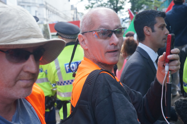 Eine Gruppe von Menschen mit einer Person mit Mütze auf der linken Seite und einem Polizisten im Hintergrund.