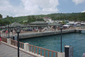 Eine breite Fl├╝sse mit einer ├ťberquerung ├╝ber Menschen unter Zelten, ein Berg mit B├Ąumen und Geb├Ąuden im Hintergrund.