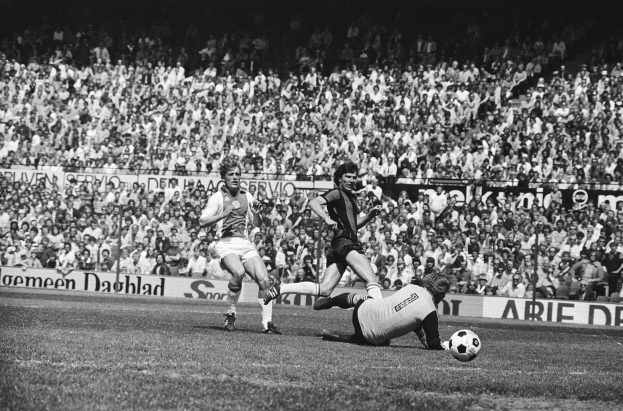Schwarzes Foto von Fussballspielern in Aktion während eines Bundesliga-Spiels zwischen Ajax und Hannover 96 in der Saison 1978-79, mit Zuschauern im Hintergrund.