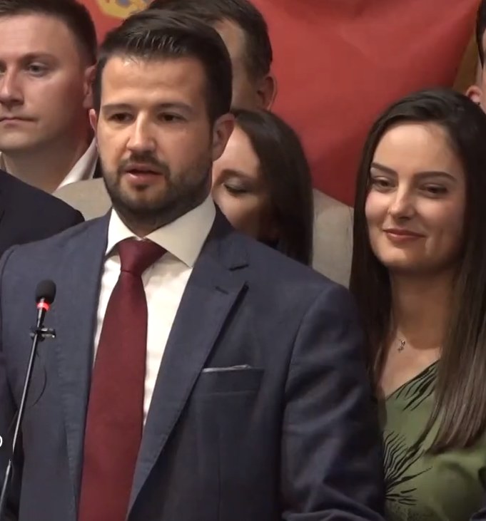 Ein Mann im Anzug spricht an einem Podium mit einem Mikrofon zu einer Menge hinter einem Banner, wahrscheinlich über ein Regierungssozialmedienverbot.