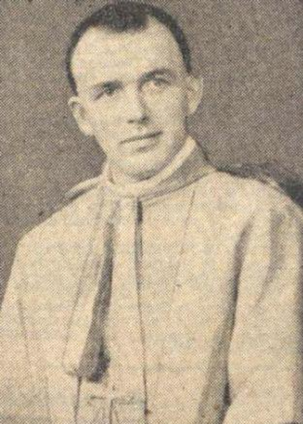 Ein Schwarz-Weiß-Foto eines Mannes in Priesterroben, der eine weiße Robe mit schwarzem Kragen und Manschetten und einen schwarzen Hut mit einer weißen Feder trägt, mit gefalteten Händen und einem ernsten Gesichtsausdruck.