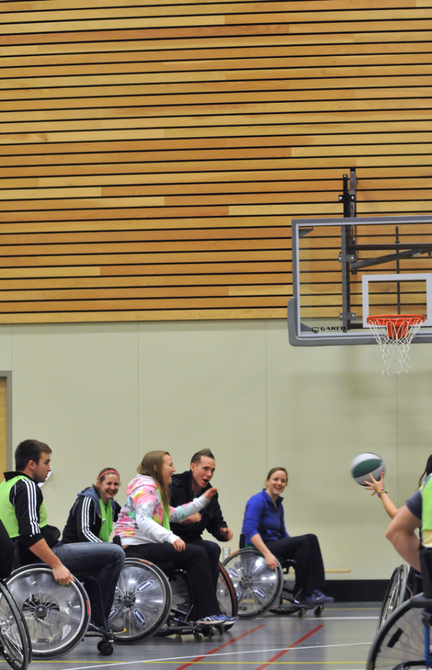 Menschen im Rollstuhl beim Basketball mit einem Korb im Hintergrund.