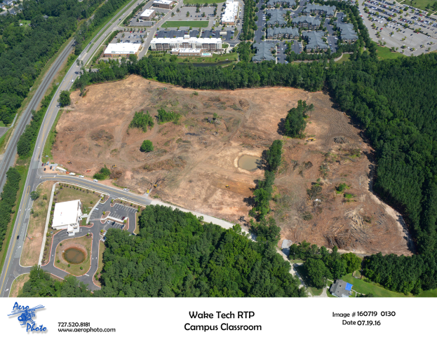 Luftaufnahme des Wake Tech RTP Campus Classroom mit Bäumen, Gebäuden, Straßen, Fahrzeugen, Gras und einem Wasserzeichen unten.