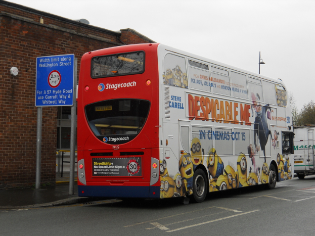 Ein wei√ües und rotes Bus steht auf einer Stra√üe mit einer roten Backsteinwand und einem blauen Warnschild im Hintergrund.
