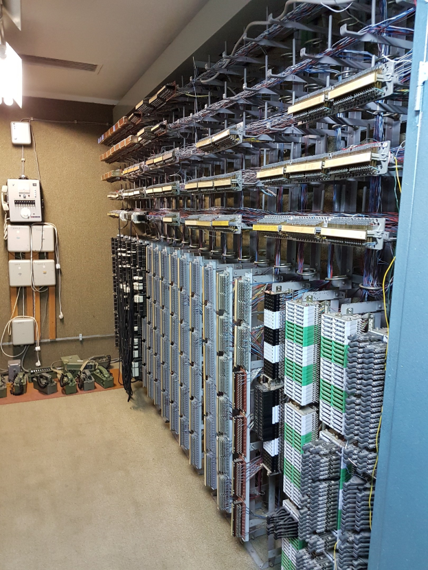 Großer Raum mit zahlreichen Kabeln und elektronischen Geräten auf dem Boden, darunter Server und Kabel, die auf ein Rechenzentrum hinweisen, mit einer Wand auf der linken Seite.