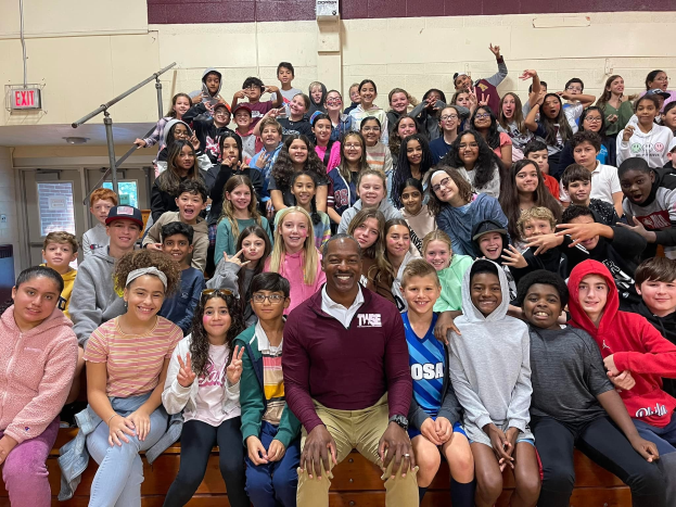 Gruppe von Schülern, die vor einer Turnhalle posieren, einige sitzen auf der Treppe und andere stehen, eine Tür und ein Ausgangsschild sind links zu sehen.