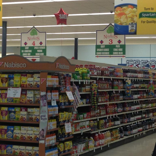 Ein Supermarkt-Innenraum mit Regalen voller Lebensmittel, Deckenleuchten und Schildern.