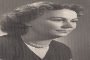 Ein Schwarz-Weiß-Foto einer Frau mit ernstem Gesichtsausdruck, die eine Kette und ein einfaches Kleid mit hohem Kragen und langen Ärmeln trägt und deren Haar zurückgebunden ist.