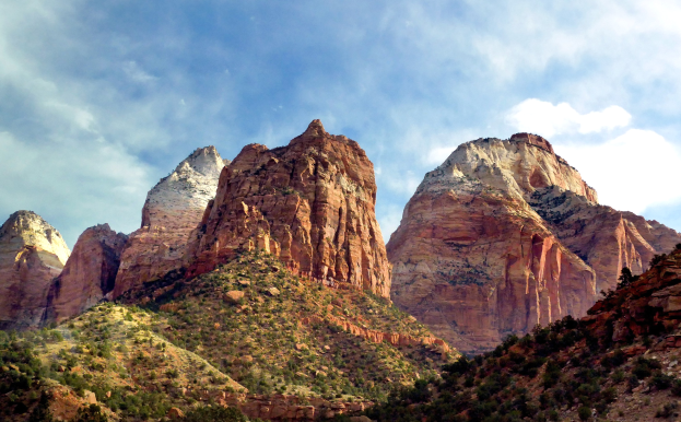 Zion National Park in Utah mit majestätischen Bergen, üppigen Bäumen, steiniger Landschaft und einem Himmel voller weißer Wolken.