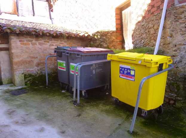 Zwei gelbe und graue Mülltonnen mit Rollen für die Trennung von Recyclingmaterial nebeneinander vor einem Gebäude mit einer Wand und einem Fenster.