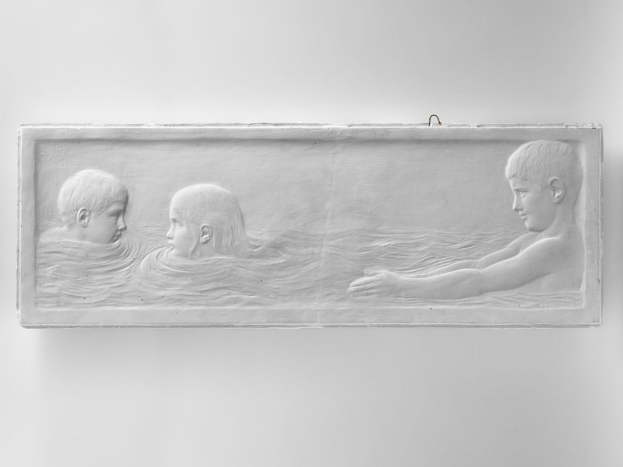Drei Kinder schwimmen in einem Gewässer, mit einer Wand im Hintergrund.