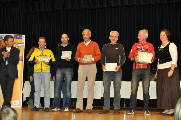 Eine Gruppe von Menschen steht auf einer Bühne und hält Zertifikate in den Händen, mit einem Banner im Hintergrund, einem Tisch zur Seite und einem schwarzen Vorhang.