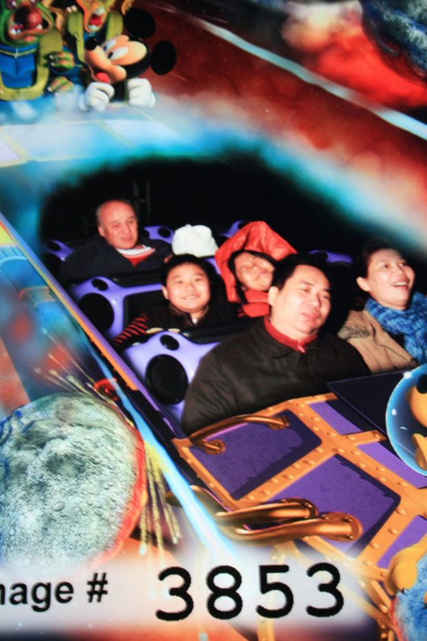 Gruppe von Menschen, die auf einer Achterbahn fahren, mit Mickey Mouse-Figuren im Hintergrund und Text unten.