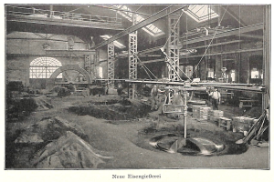 Altes Schwarz-Weiß-Foto einer Fabrik mit Arbeitern an einer Maschine, umgeben von Metallstangen und -pfählen, mit der Beschriftung "Neue Eisenglebeerei, die erste Fabrik in Deutschland" unten.