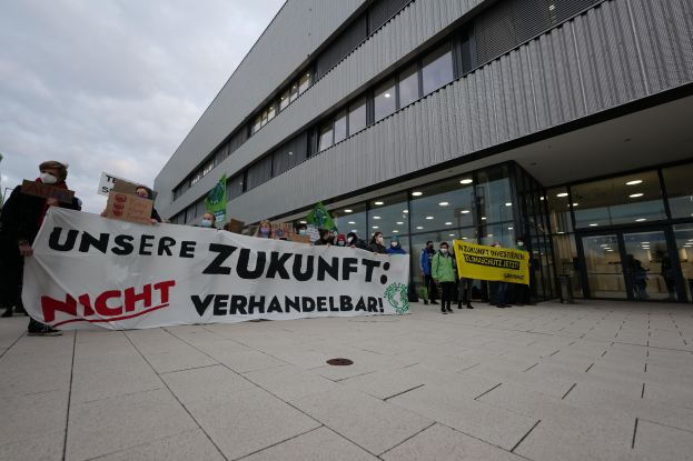 Eine Gruppe von Menschen hält ein Transparent mit der Aufschrift "Unsere Zukunft Verhandelbar" ("Wir haben keine Angst zu kämpfen") vor einem Glasgebäude bei Nacht.